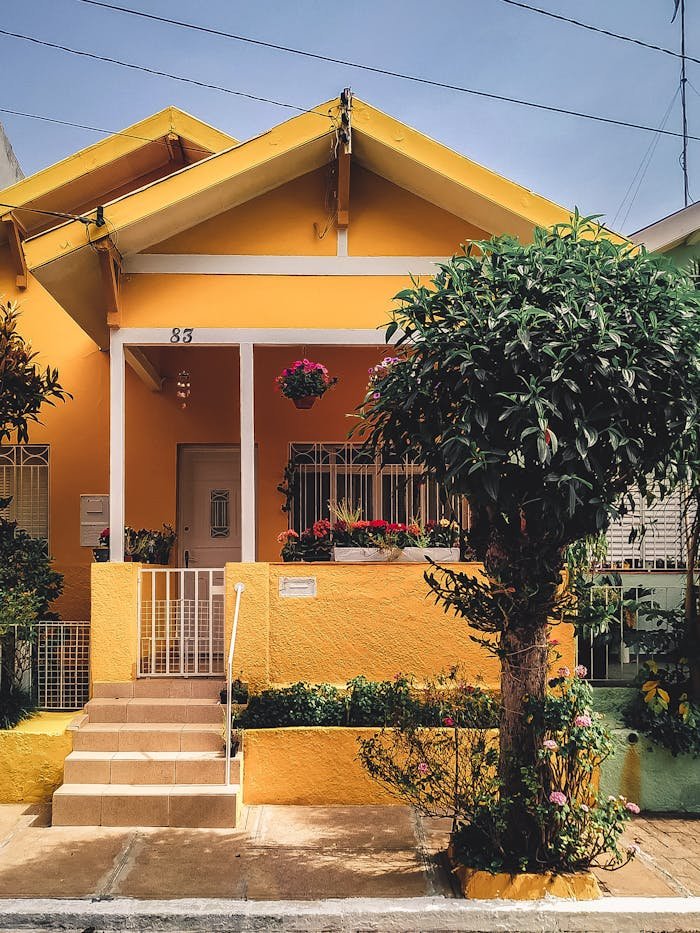 Bright yellow house with lush garden, vibrant flowers, and welcoming porch entrance.